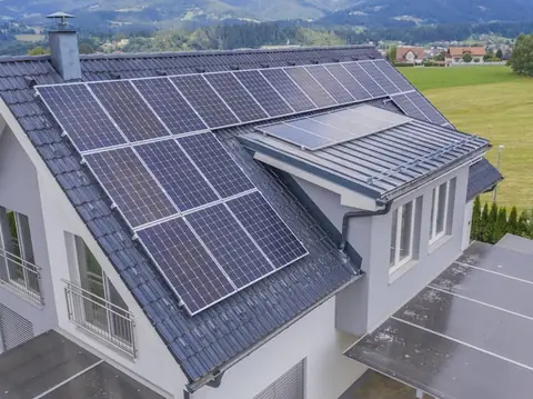 Casă particulară cu panouri fotovoltaice pe acoperiș, văzută de sus, printre câmpuri verzi
