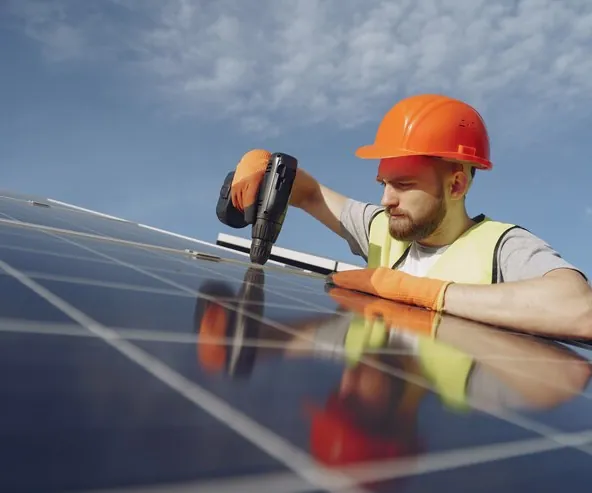 Montator cu cască portocalie care fixează cu mașina de înșurubat un panou fotovoltaic